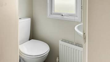 Ein kleines, sauberes Badezimmer mit Toilette, Fenster und Heizkörper.