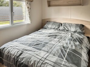 A bed with a grey and white checkered bedspread, a wooden headboard, and a window with curtains.