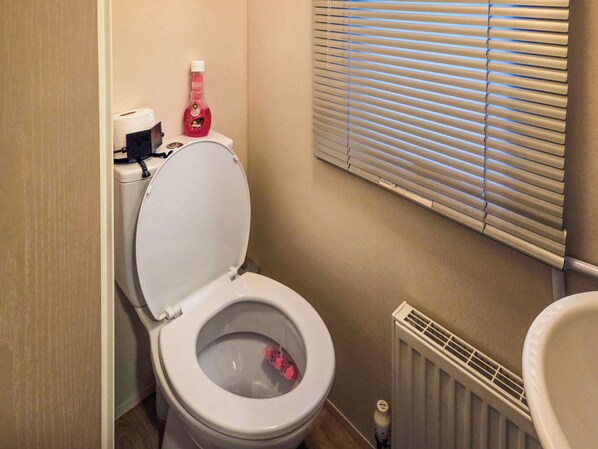 Een badkamer met een toilet, een fles vloeibare zeep en een raam met jaloezieën.