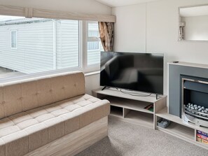 Een woonkamer met een beige bank, een flatscreen televisie op een standaard, een open haard en een raam met jaloezieën.