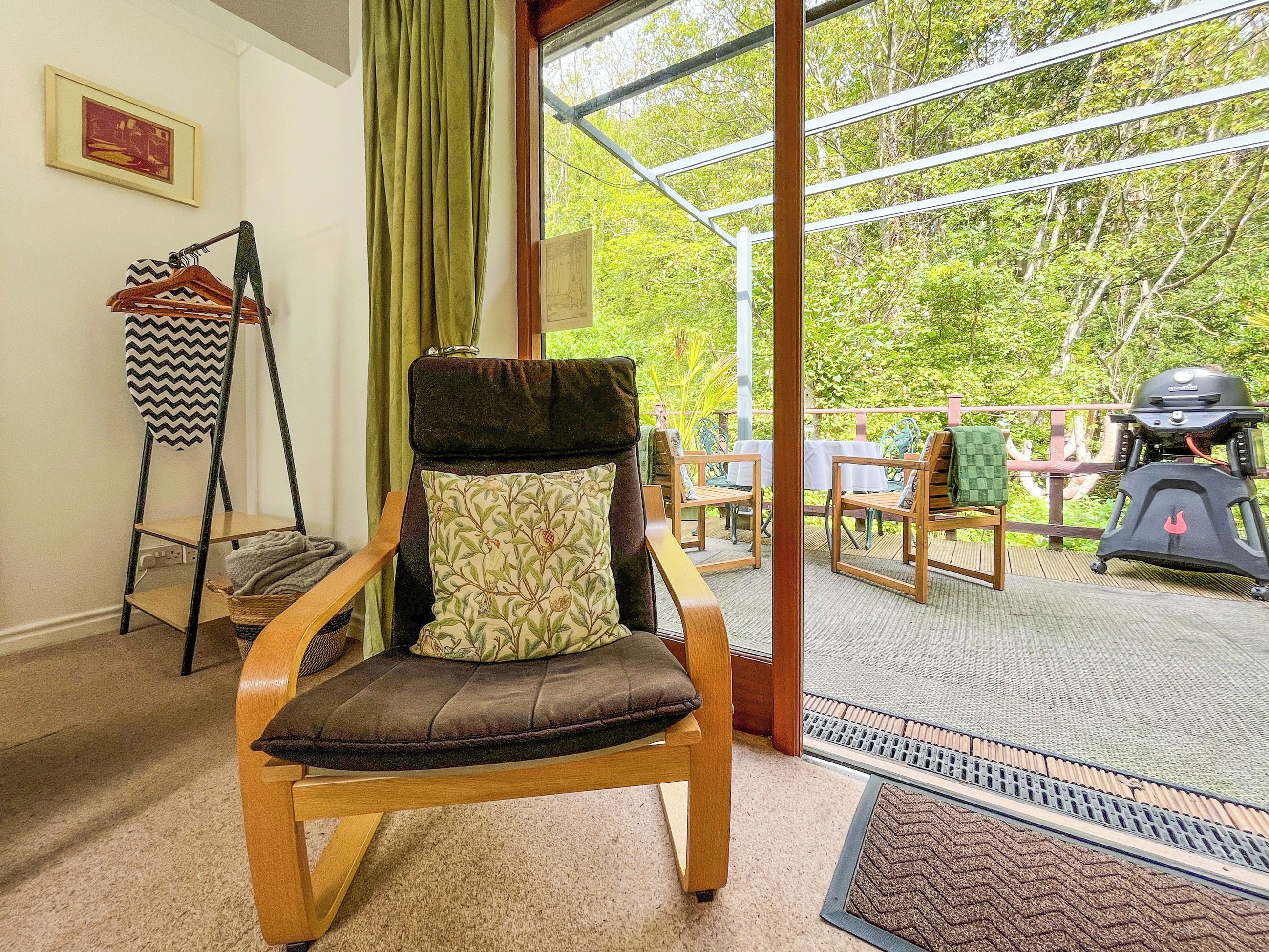 Une chaise en bois avec un coussin, un portant en métal avec des cintres, et une vue sur un patio extérieur avec un barbecue.