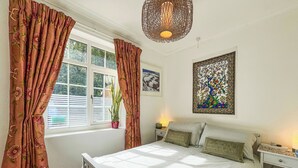 Ein Schlafzimmer mit einem Bett, Vorhängen, einem Fenster, einer Wandlampe und einem gerahmten Kunstwerk.