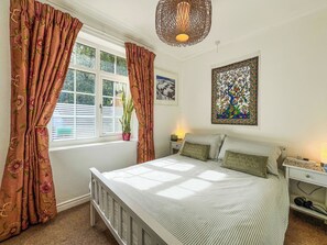 Ein Schlafzimmer mit einem Bett, Vorhängen, einem Fenster, einer Wandlampe und einem gerahmten Kunstwerk.