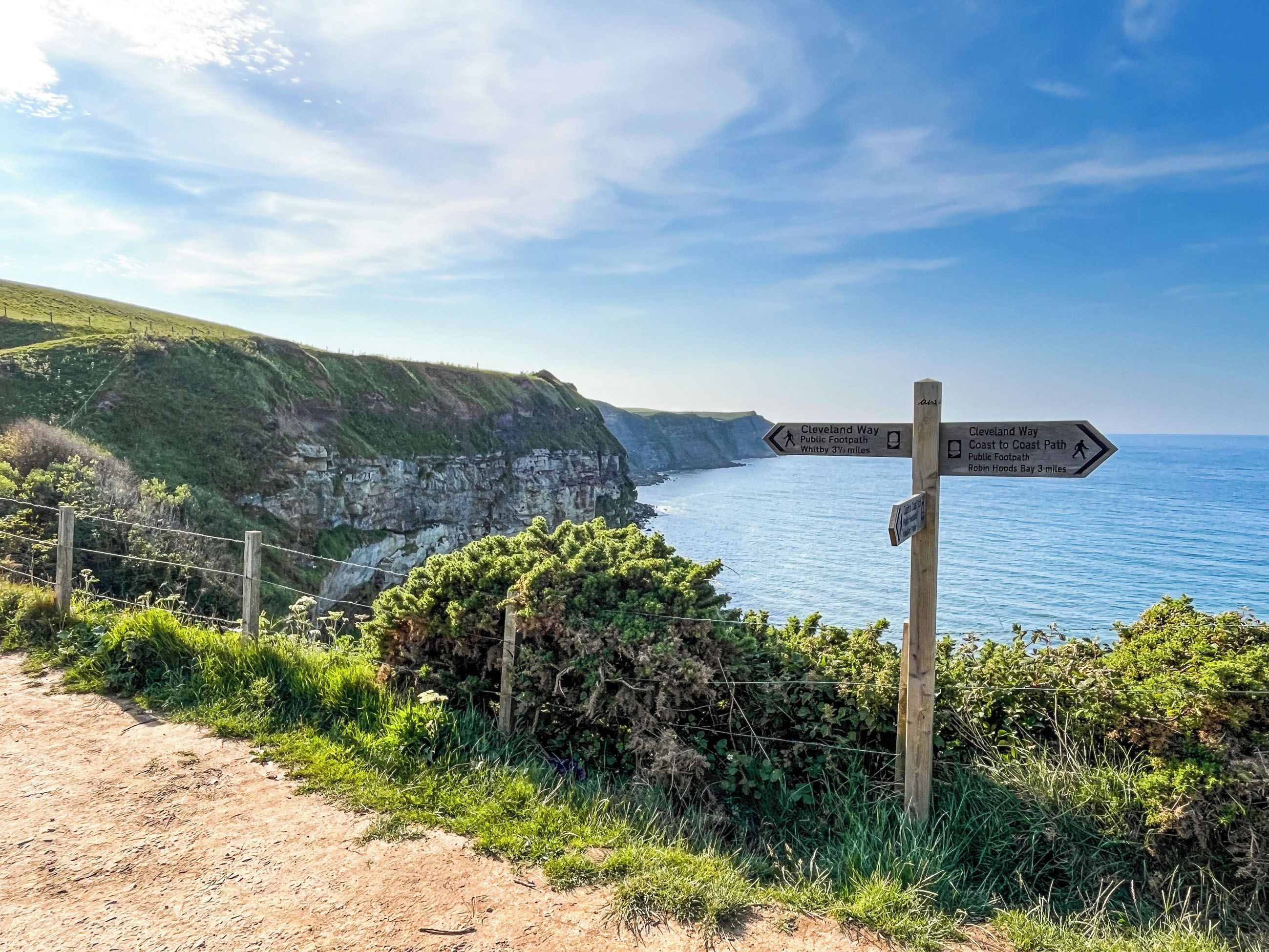 Een richtingswijzer met routes naar Cleveland Way en Robin Hood's Bay, met uitzicht op een kustlandschap.