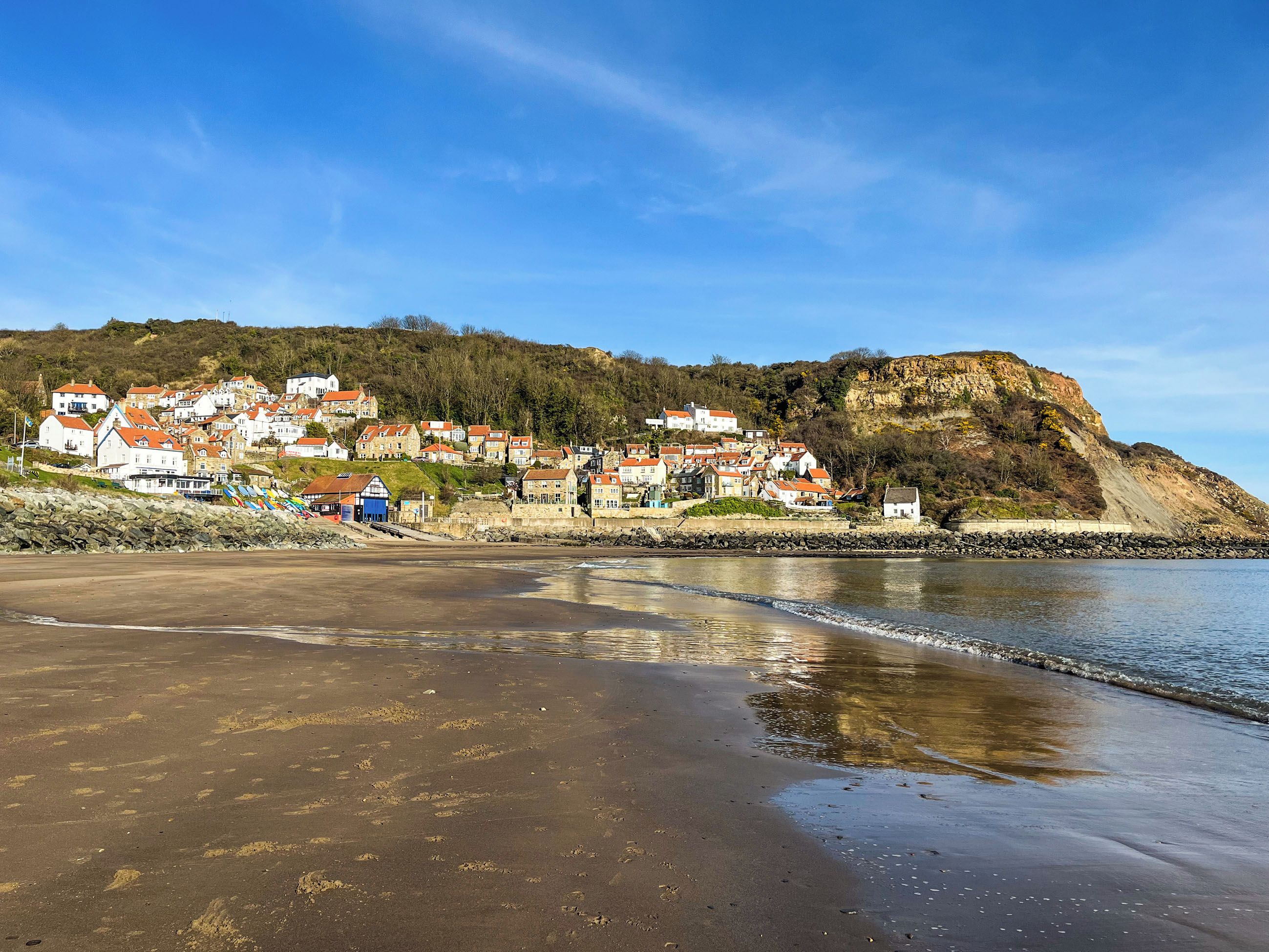 A coastal town with houses on a hillside, a sandy beach, and a rocky shoreline.
