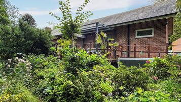 A brick building with a metal roof, surrounded by dense greenery and flowering plants.