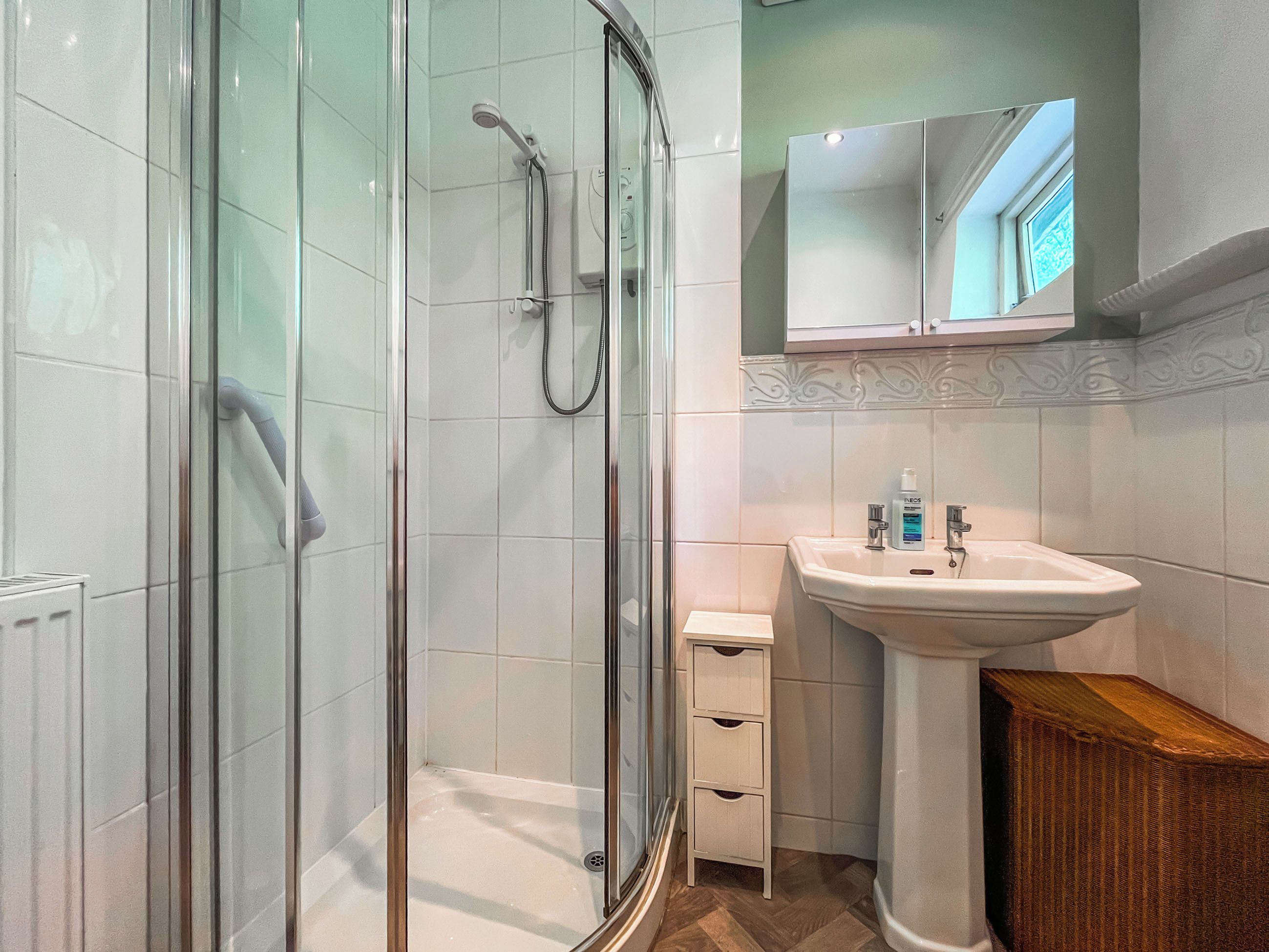 A modern bathroom with a glass-enclosed shower, a white sink with a mirror above, and a small wooden cabinet.