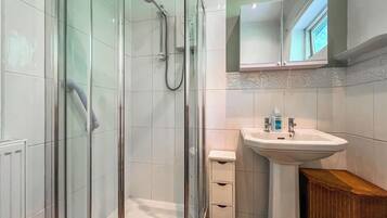 A modern bathroom with a glass-enclosed shower, a white sink with a mirror above, and a small wooden cabinet.