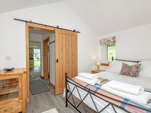 Ein Schlafzimmer mit einem Bett, einem Holzschrank, einem Schreibtisch und einem Fenster mit Blick ins Grüne.