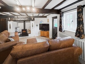 A living room with a fireplace, leather sofas, a television, and a window with curtains. - 5 bedroom accommodation in Oswestry (Shropshire)