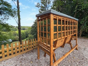 A wooden gazebo with a sloped roof, surrounded by a wooden fence, set on gravel with a view of a green landscape. - 5 bedroom accommodation in Oswestry (Shropshire)