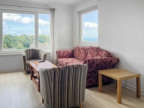 A room with a sofa, two chairs, a wooden table, and large windows offering a view of trees and the sky. - 3 bedroom accommodation in Paignton (Paignton)