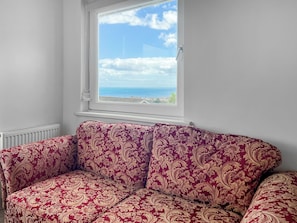 A room with a red patterned sofa, a white radiator, and a window with a view of the sea. - 3 bedroom accommodation in Paignton (Paignton)