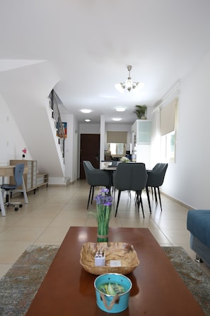 A modern living room with a dining area, a staircase, and a kitchen in the background. - Elysia park - Charming 2BR Townhome with Pool, Gym, Free parking-Paphos central (Pafos)