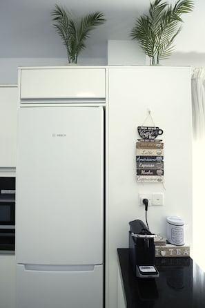 A kitchen with a white Bosch refrigerator, a coffee machine, and a wall-mounted sign listing coffee types. - Elysia park - Charming 2BR Townhome with Pool, Gym, Free parking-Paphos central (Pafos)