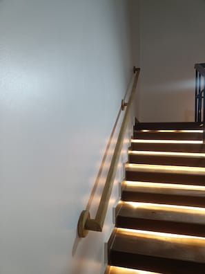 A staircase with a handrail and steps illuminated by underglow lighting.