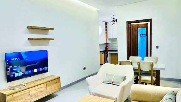 Een moderne woonkamer met een flatscreen televisie, houten meubels, een bank en een eethoek.