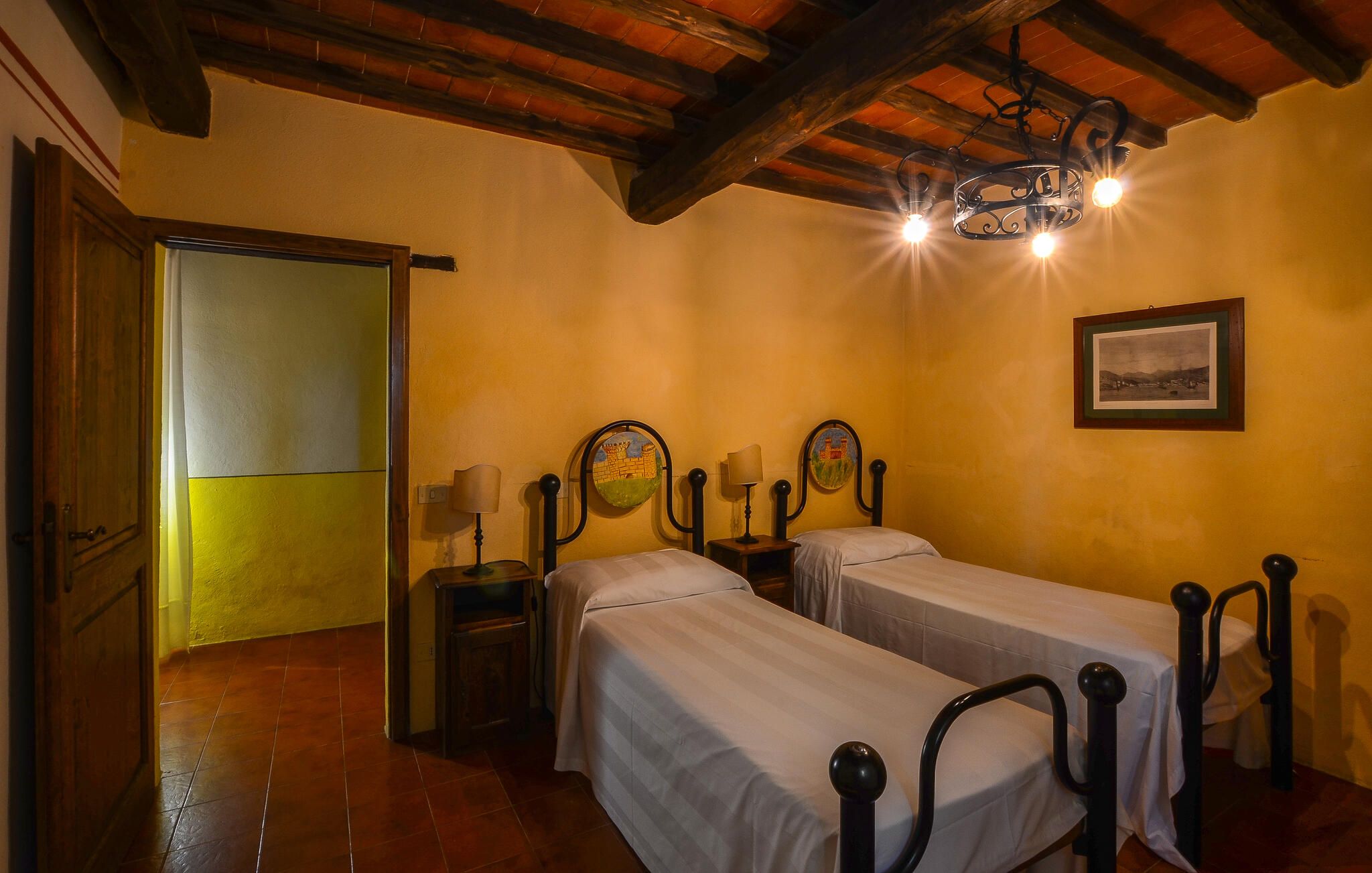 Una habitació amb dos llits, sostre de fusta, una porta, paret amb un quadre i un penjador.