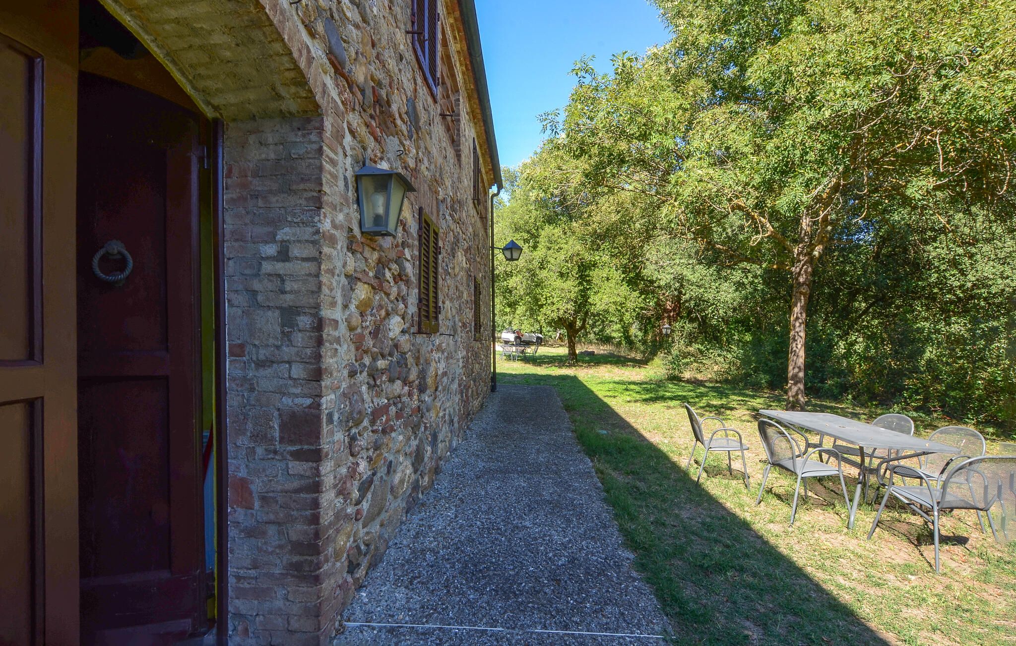 Un bâtiment en pierre avec un chemin de gravier menant à une table et des chaises installées à l’extérieur.