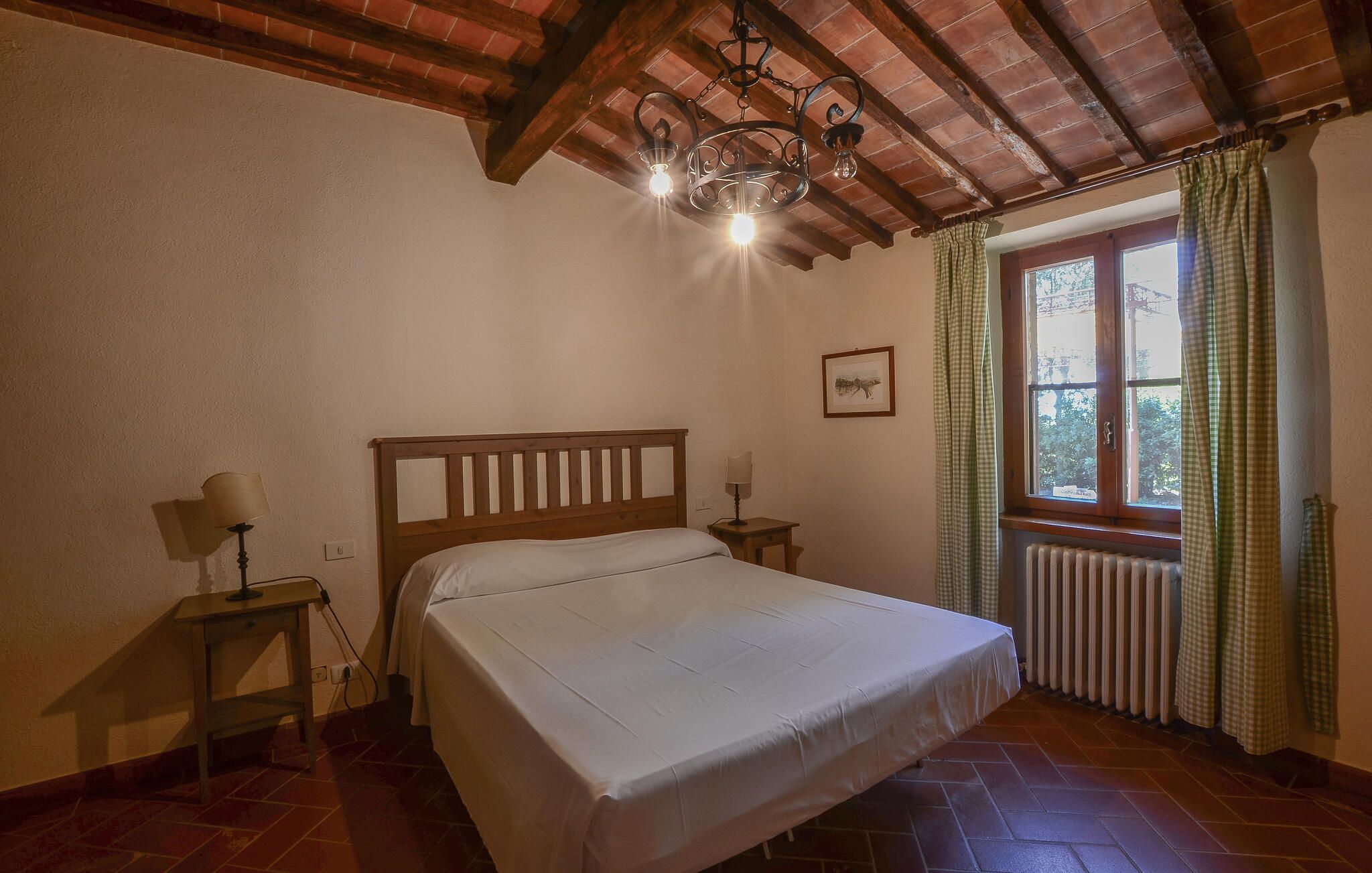 Ein Schlafzimmer mit einem hölzernen Bett, einem Heizkörper, einem Fenster mit Vorhängen und einer Chandelüster.
