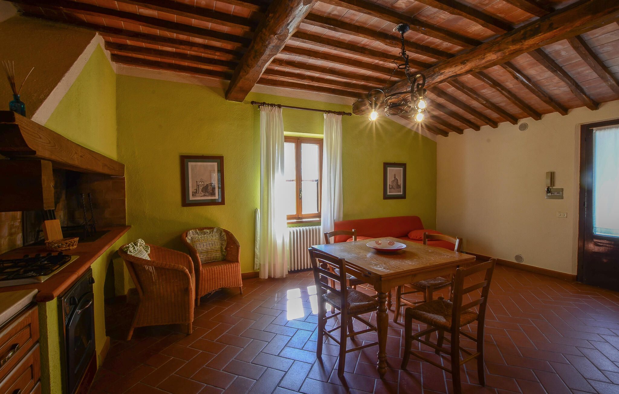 Un comedor con mesa y sillas de madera, un sofá rojo y una cocina con estufa y alacenas.