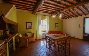A dining area with a wooden table and chairs, a red sofa, and a kitchen area with a stove and cabinets. - Beautiful home in Murlo with house a panoramic view (Murlo)