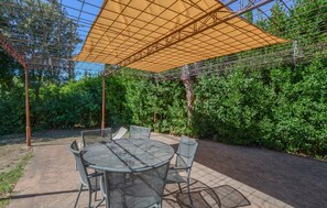 An outdoor patio with a round metal table and chairs, a pergola with a mesh roof, and dense green foliage in the background. - Beautiful home in Murlo with house a panoramic view (Murlo)