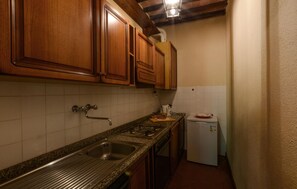 Een keuken met houten kastjes, een RVS spoelbak, een fornuis en een witte koelkast.
