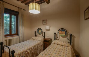 Een slaapkamer met twee enkele bedden, een raam met gordijnen, een radiator en een hanglamp.