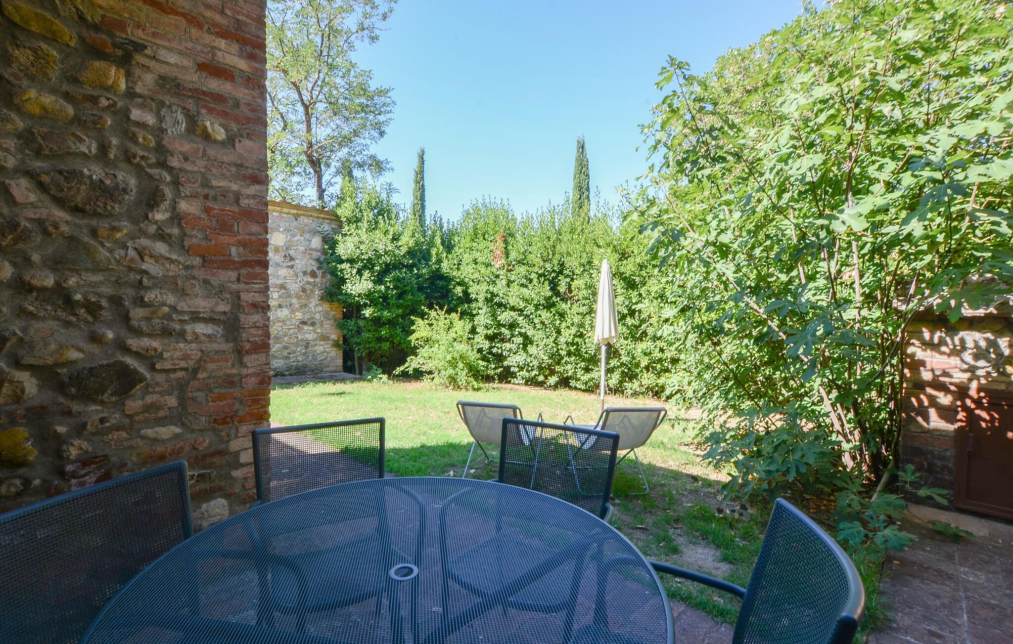 A patio with a round table and chairs, surrounded by greenery and a stone wall.