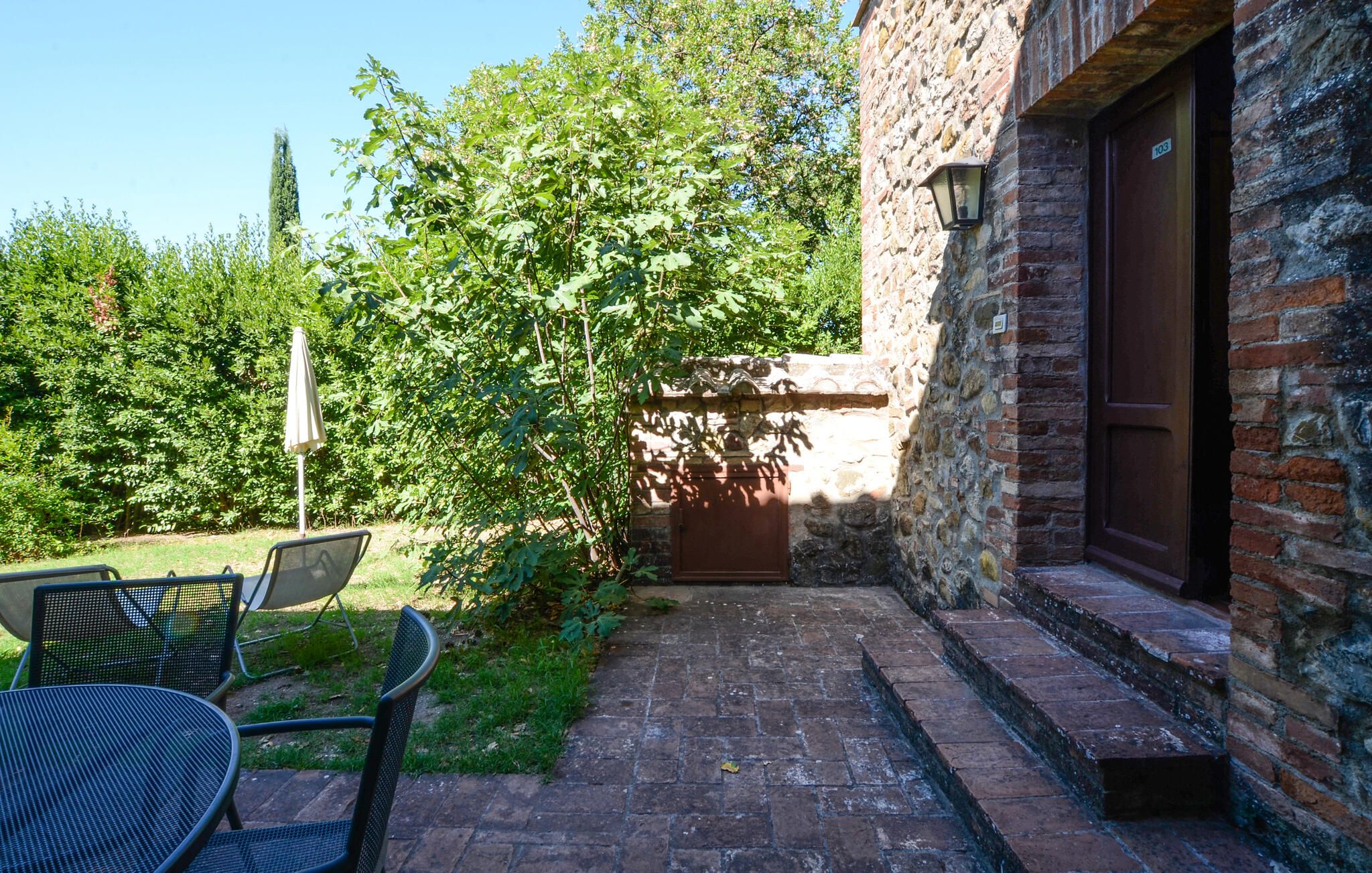 Un bâtiment en pierre avec une porte en bois, un chemin pavé et du mobilier d’extérieur.