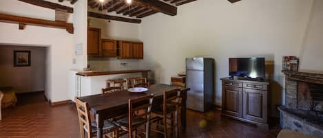 A kitchen with wooden cabinets, a refrigerator, a dining table with chairs, and a television on a cabinet.