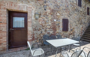 A rustic stone building with a wooden door, a small window, and a metal table with chairs outside. - Beautiful home in Murlo with outdoor swimming pool (Murlo)