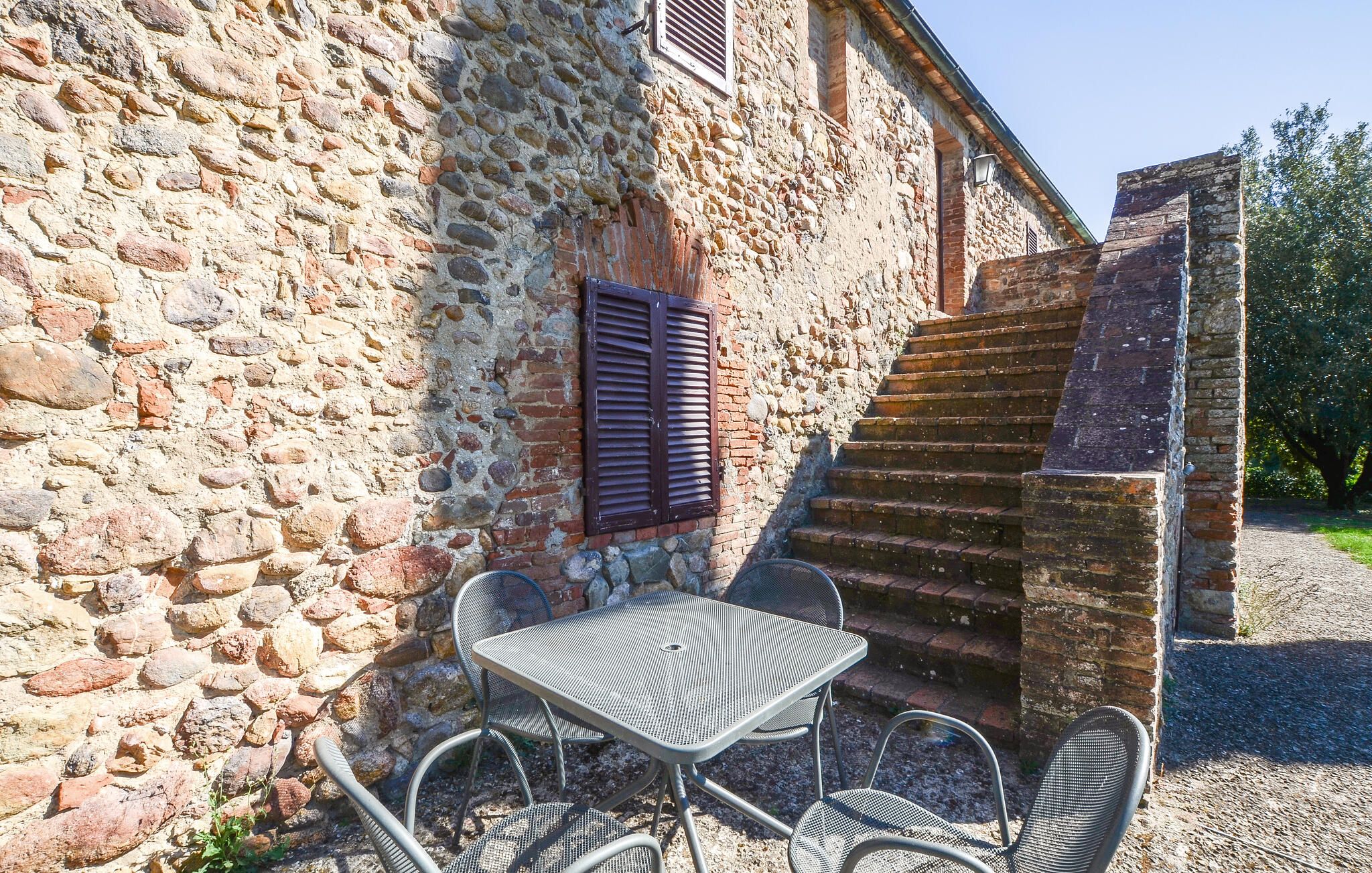 Ein Steinhaus mit einer Treppe, die zu einer höheren Ebene führt. Draußen steht ein Metalltisch mit Stühlen.