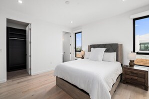 Ein Schlafzimmer mit Bett, Nachttisch, Lampe und Blick ins Freie.