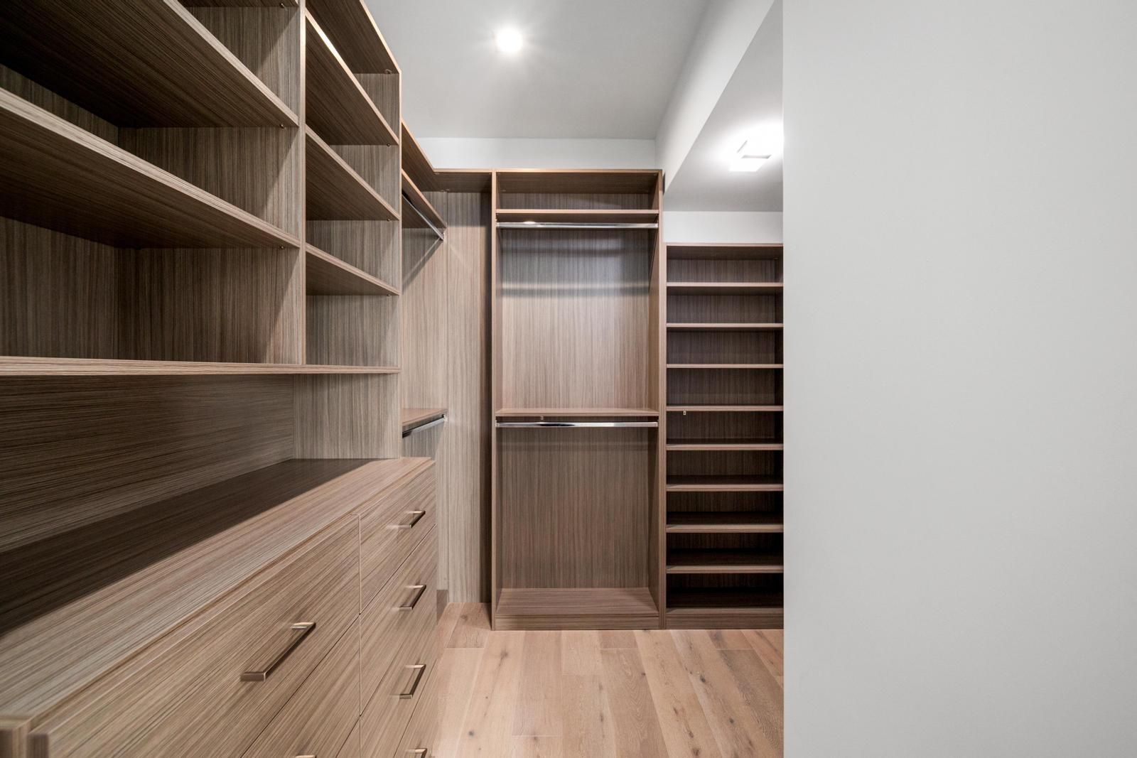 Um closet espaçoso com prateleiras abertas, porta com espelho e piso de madeira.