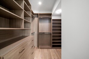 Um closet espaçoso com prateleiras abertas, porta com espelho e piso de madeira.