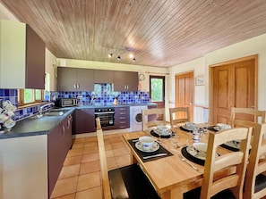 Cozinha com teto de madeira, área de jantar com mesa posta para quatro e janela com cortinas.