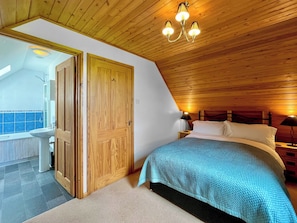 A bedroom with a wooden ceiling, a bed with a blue quilt, a nightstand with a lamp, and a wooden door leading to a bathroom. - Hardy Chalet - UK47157 (West Stour, near Gillingham)