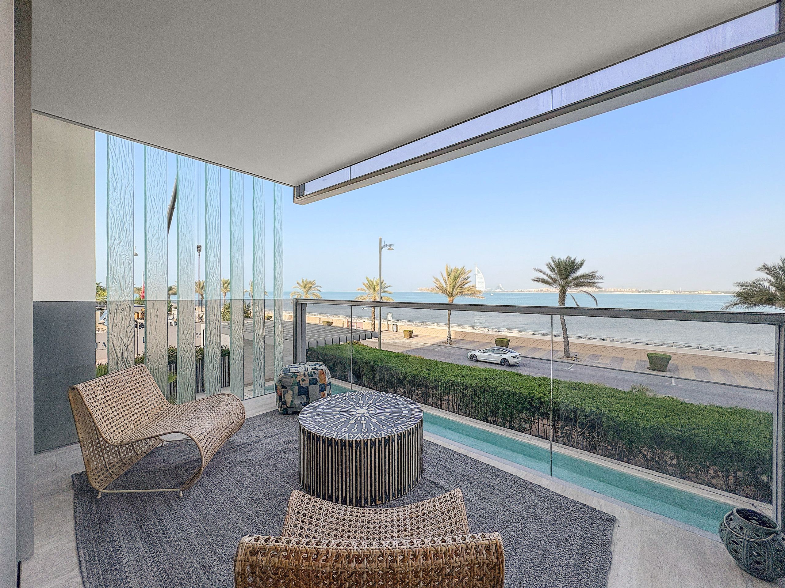 A balcony with wicker furniture, a round table, and a view of the sea and palm trees.