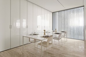 A modern dining area with a glass table, white chairs, and a view through a large window. - Muraba Dia | Ultra-Luxe Sea View Residence (Dubai)