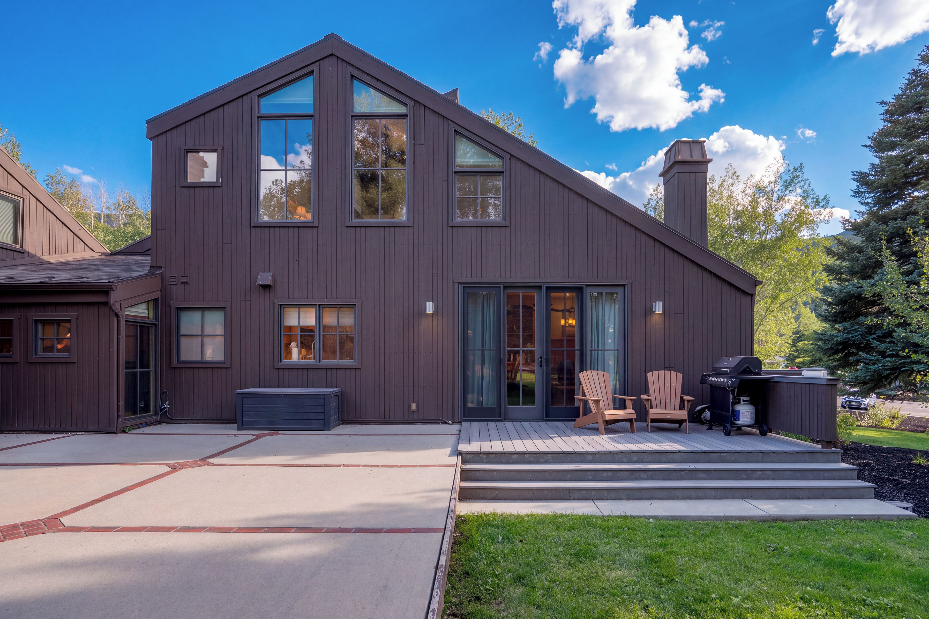 A modern two-story house with a large deck, a barbecue area, and a covered outdoor seating space.