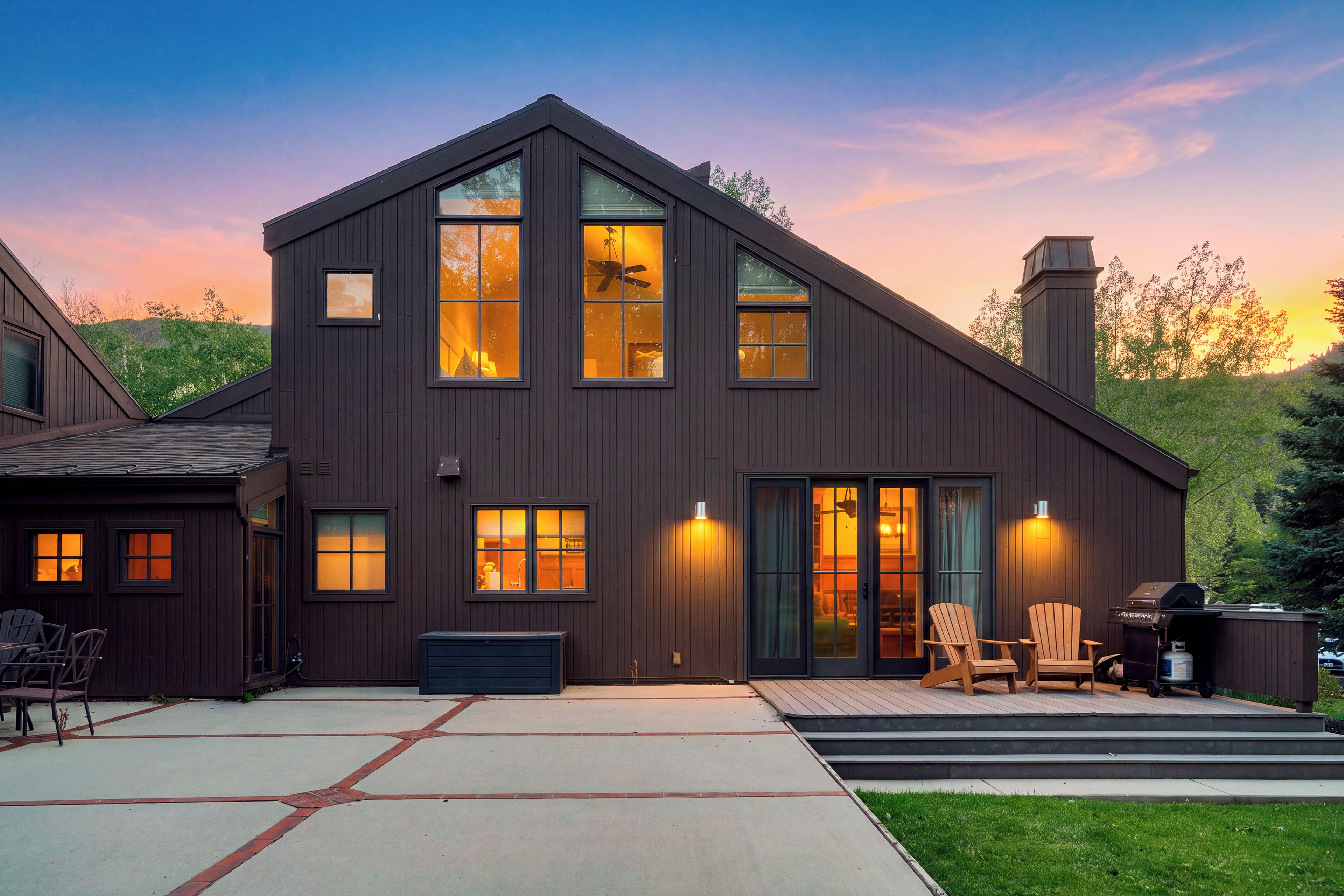 A modern two-story house with a large front porch, a garage, and a deck area with outdoor seating.