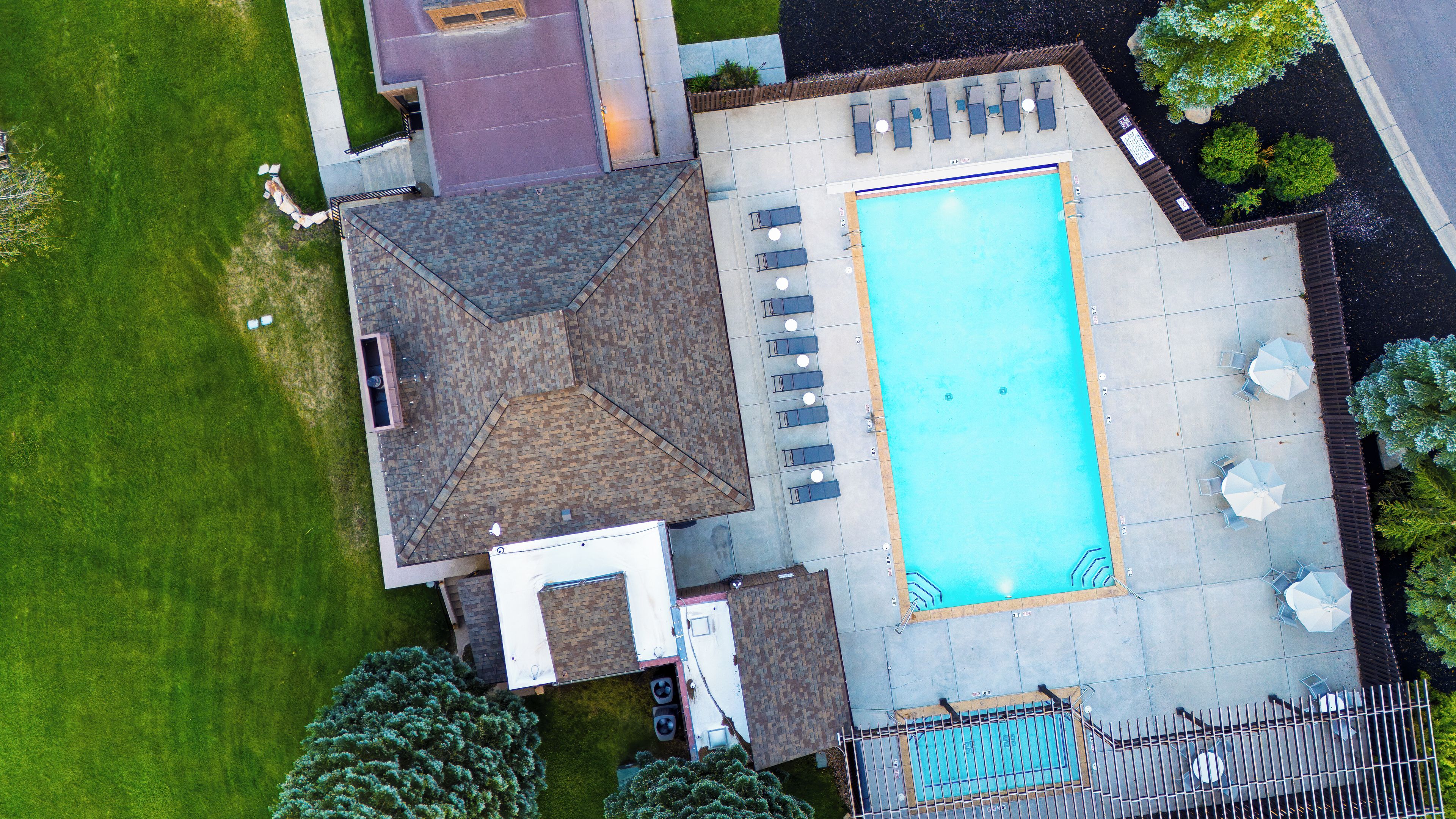An aerial view of a residential property with a swimming pool, patio furniture, and a fenced garden area.