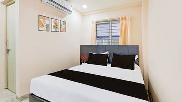 Quarto de hotel com cama, ar condicionado, janela com cortinas e porta.