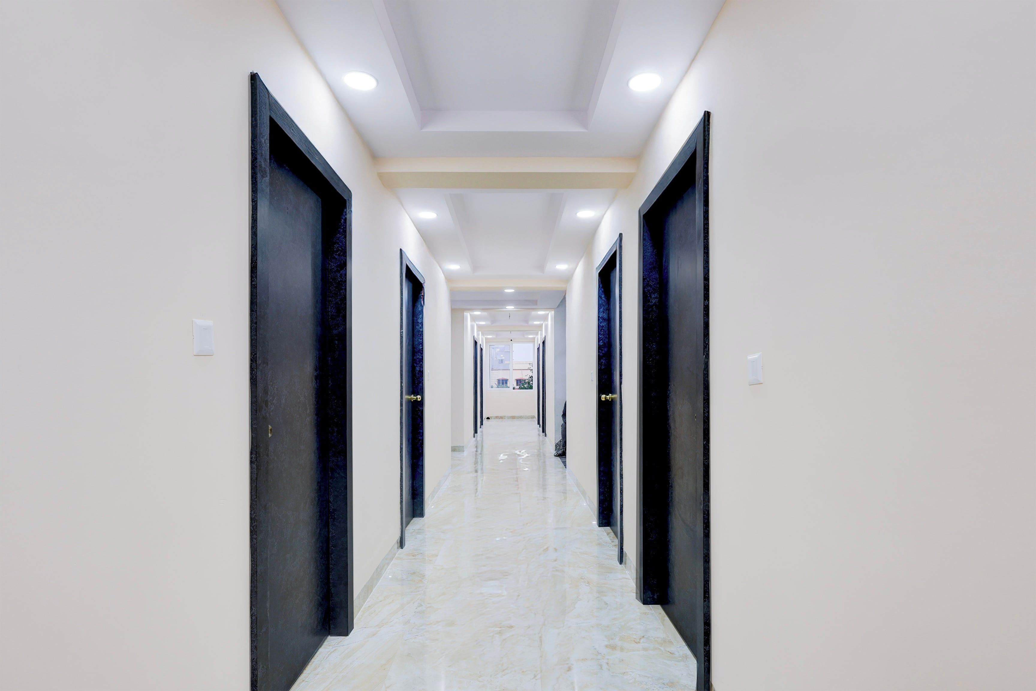 A corridor with doors on both sides, recessed lighting, and a marble floor.