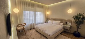 Ein Hotelzimmer mit Bett, Nachttischen, einem Sessel, einem Fernseher und einer Topfpflanze.