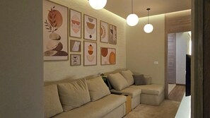 Ein Wohnzimmer mit einem beigefarbenen Ecksofa, einem Flachbildfernseher und abstrakten Wandbildern.
