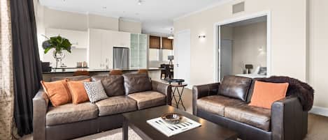 A modern living room with leather sofas, a coffee table, and a kitchen in the background.