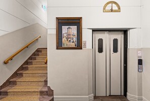 A staircase with a handrail, a framed picture above it, and an elevator door with a control panel. - The Ocean Views Suite (Napier)